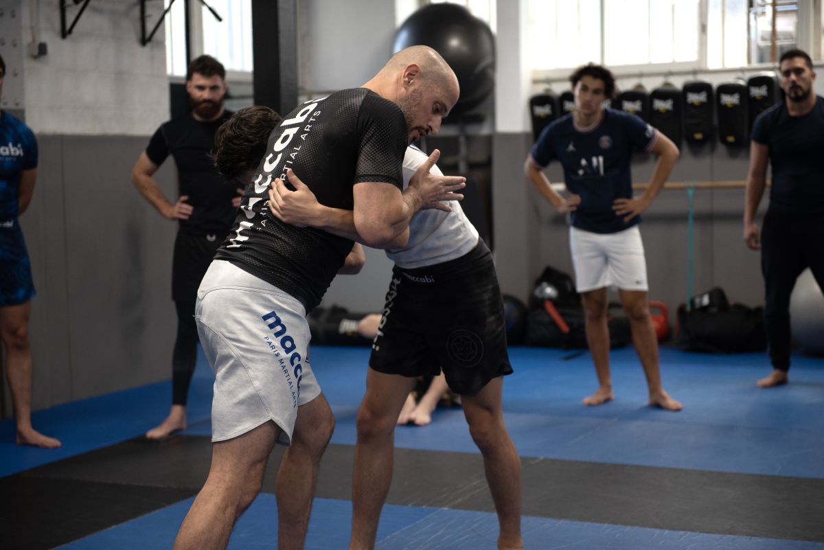 Débutants en MMA apprenant une technique de clinch lors d’un entraînement, illustrant les bénéfices physiques et mentaux du fait de commencer le MMA.